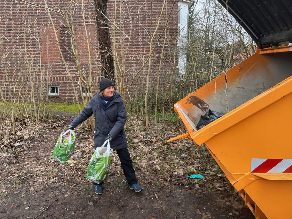 Freiwillige Helferin trägt volle Müllbeutel zum orangefarbenen Container bei der Aktion Ottenbeck räumt auf 2026
