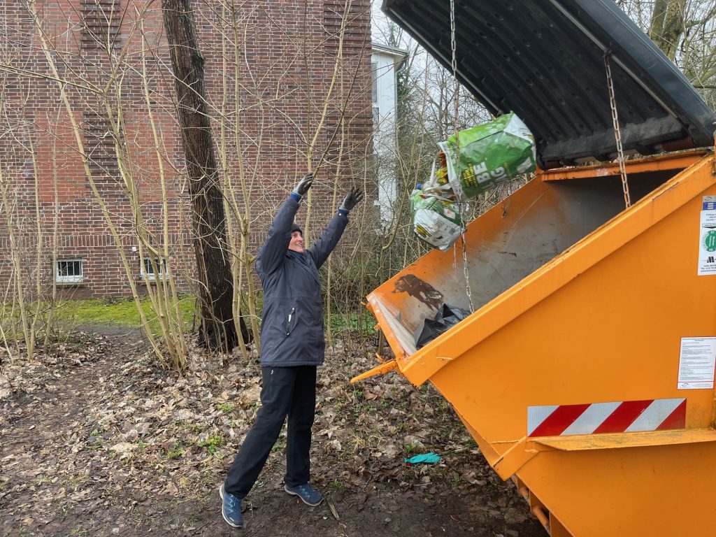 Helferin wirft einen vollen Müllbeutel in einen orangefarbenen Container bei der Aktion Ottenbeck räumt auf 2026