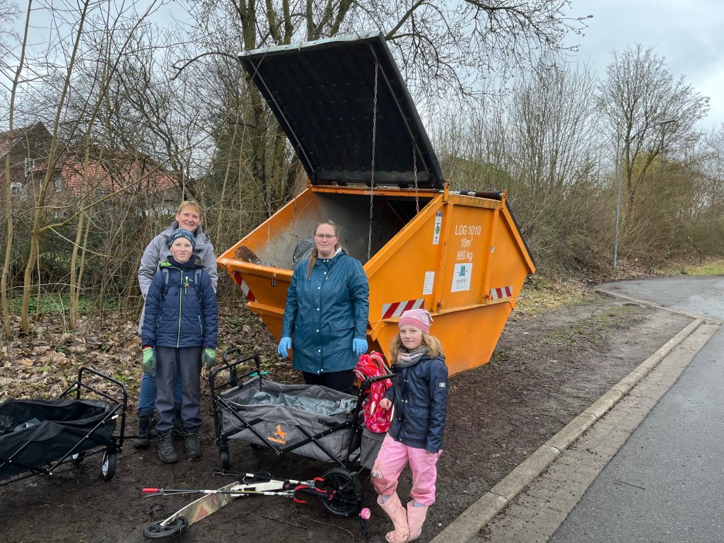 Familie mit Kindern steht mit Bollerwagen und gesammeltem Müll vor dem Container bei der Aktion Ottenbeck räumt auf 2026